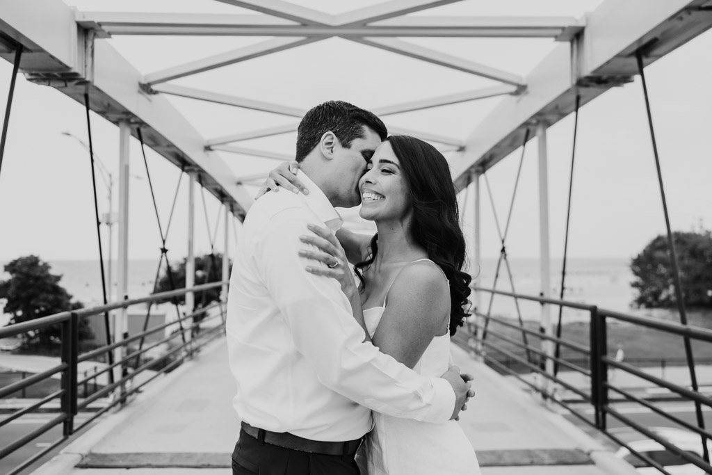 Black and white photo of engaged couple embracing and smiling on a bridge in Lincoln Park\