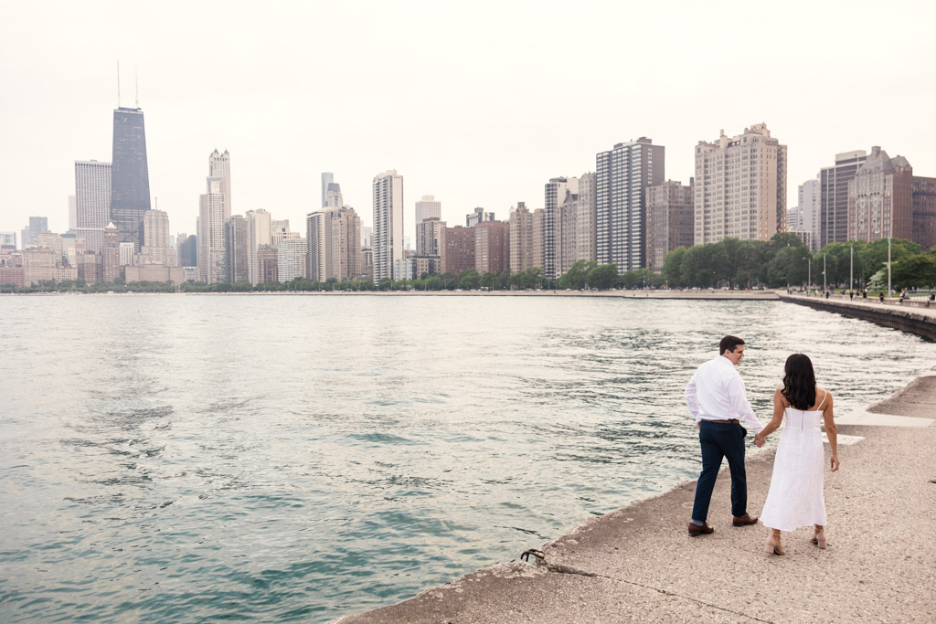 Engaged couple walks along the lakefront at North Avenue Beach with downtown Chicago in the background on a cloudy day