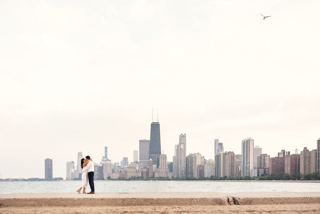 A couple kisses on the shore of Lake Michigan at North Avenue Beach in Lincoln Park with Chicago skyline in the background