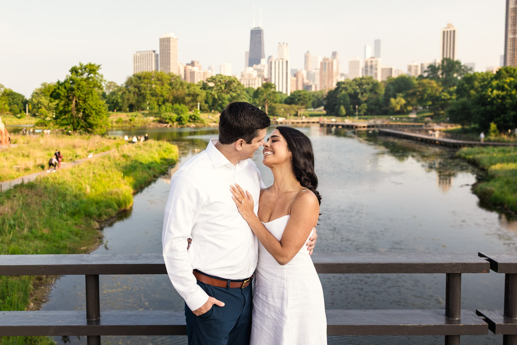Candid photo of couple smiling at each other on a bridge in Lincoln Park with Chicago skyline in the background during spring engagement session