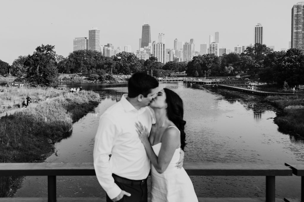 Creative black and white photo of engaged couple kissing on a bridge in Lincoln Park with Chicago skyline in the background