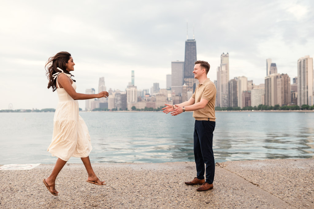 Woman in white dress jumps toward man with open arms on a North Avenue Beach pier with the Chicago skyline in the background