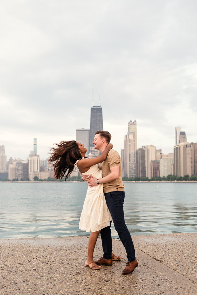 A couple embraces and laughs by the waterfront with the city skyline in the background, enjoying beautiful Chicago weather.
