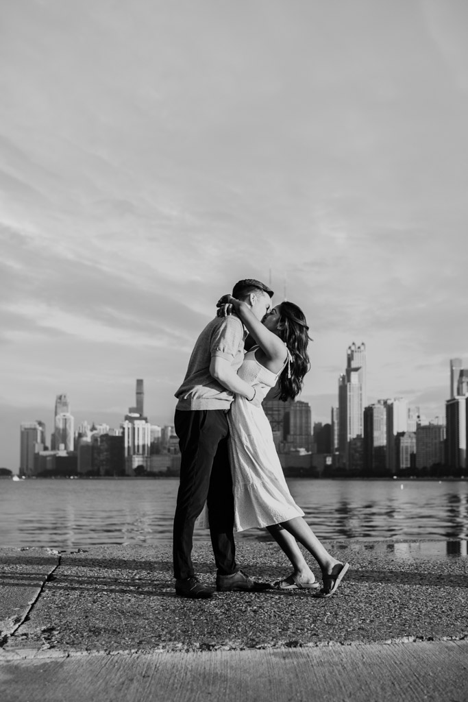 Blakc and white photo of engaged couple kissing by Lake Michigan with the Chicago skyline in the background