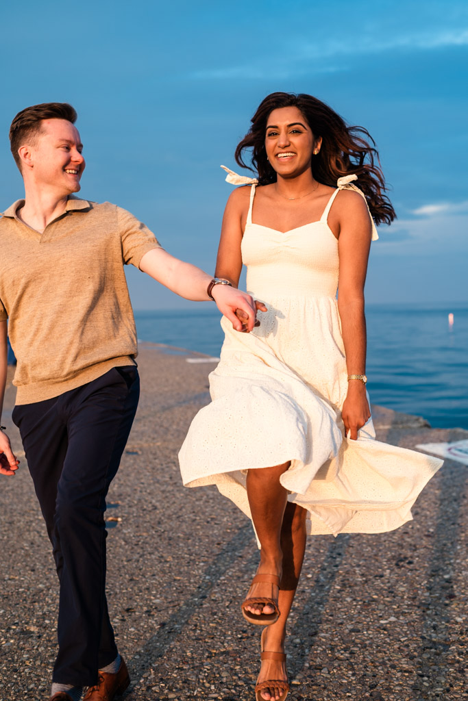 Happy engaged couple walks hand in hand along Lake Michigan at North Avenue Beach at sunset