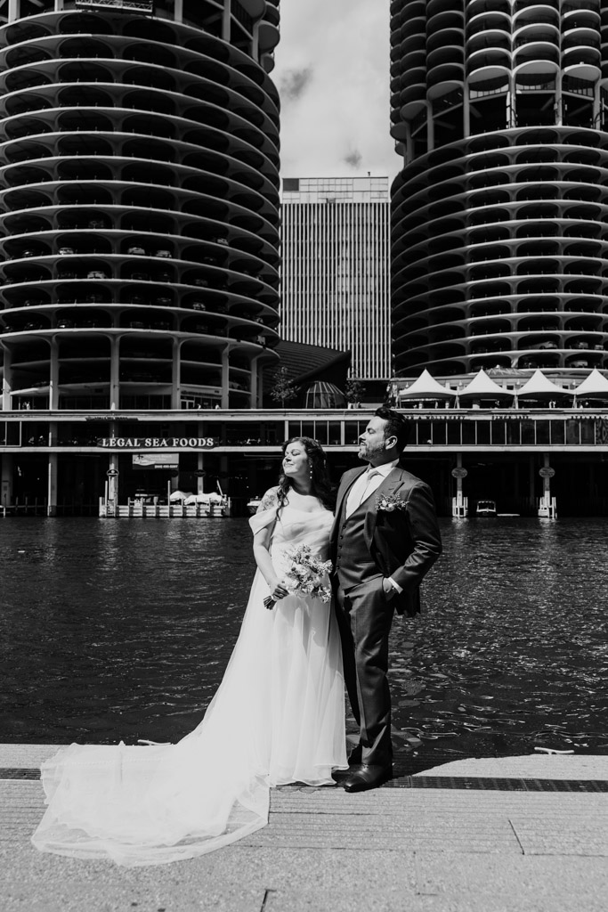 Black and white photo of bride and groom standing by the Chicago River with the Marina Towers in the background