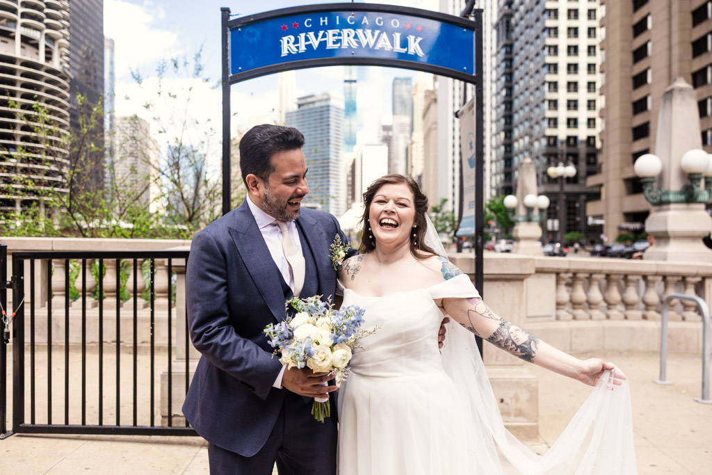 A joyful bride and groom laugh together by the Chicago Riverwalk efore their Osteria Via Stato wedding celebration