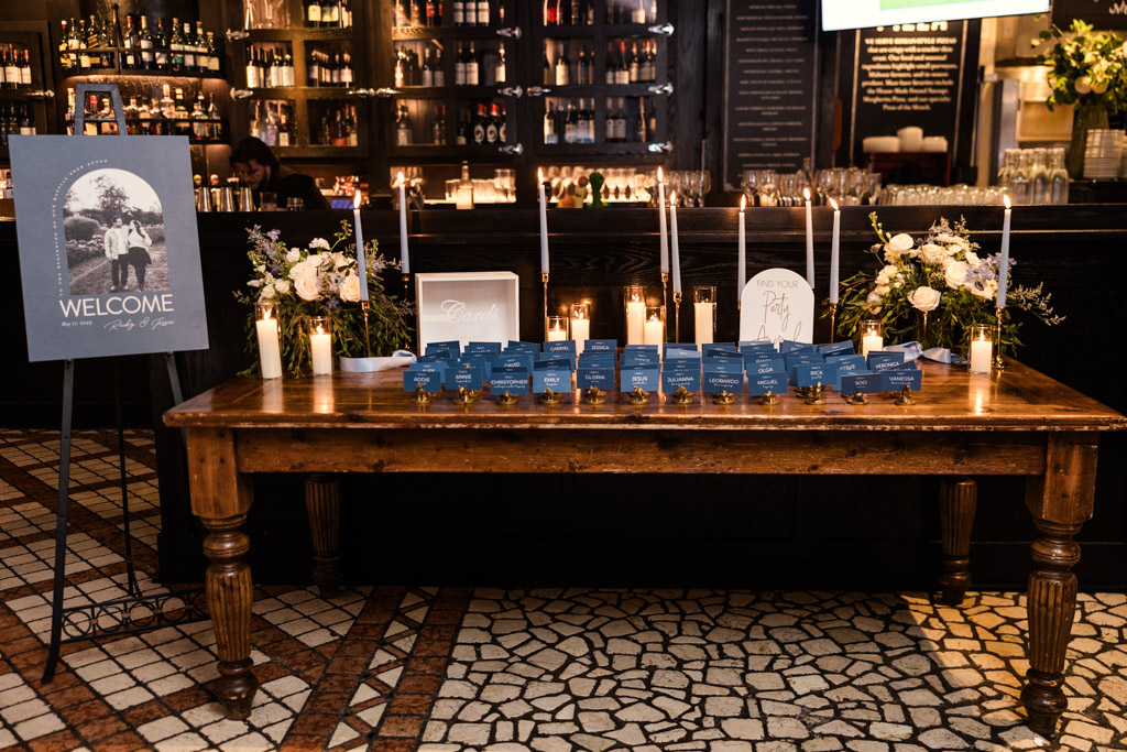 Welcome sign and wooden table at Osteria Via Stato features blue place cards, candles and flowers