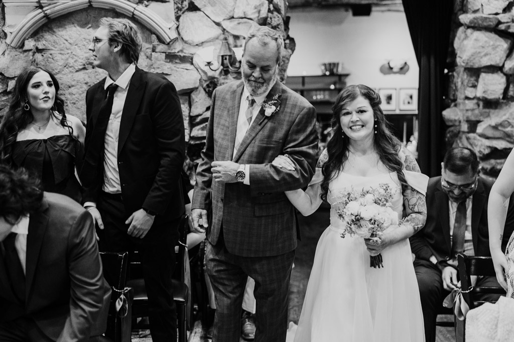 Bride in white dress walks down the aisle arm-in-arm with her father at Osteria Via Stato