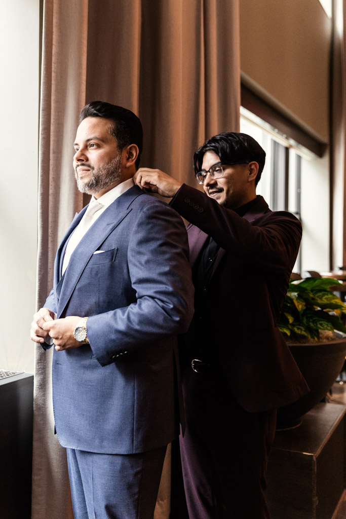 Best Man adjusts the groom's collar as they prepare for wedding celebration at Osteria Via Stato