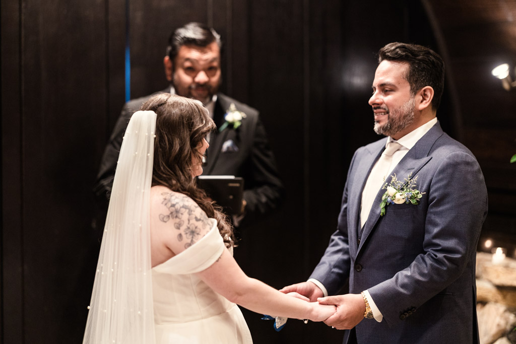 Bride and groom holding hands during their wedding ceremony at Osteria Via Stato, officiant standing behind them