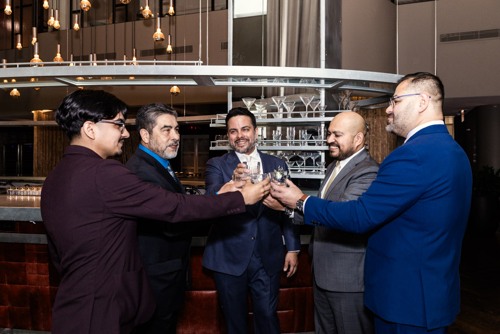 Groom and groomsmen in suits clink glasses together in a toast at Virgin Hotels Chicago