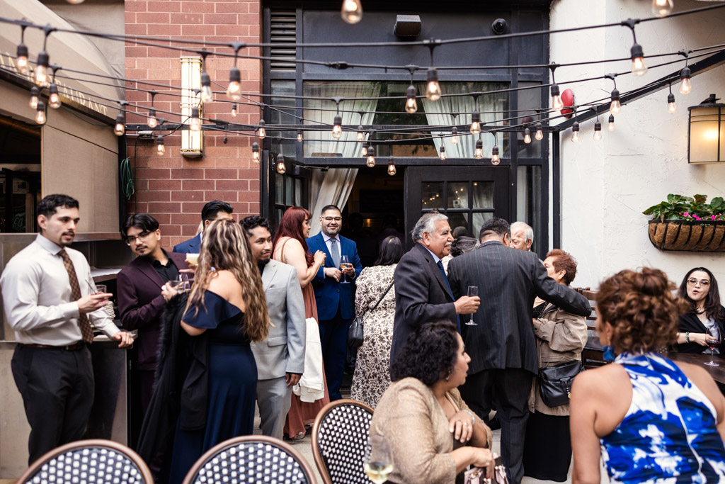 Guests in formal attire gather and chat under string lights during cocktail hour at Osteria Via Stato