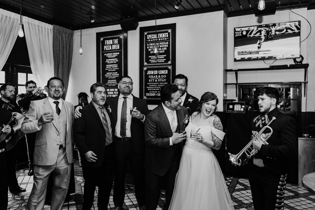 Black and white photo of bride and groom laughing with guests and musicians at Osteria Via Stato