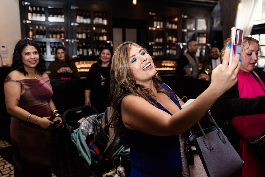 A woman in a blue dress records the bride and groom singing along with the band at Osteria Via Stato on her phone