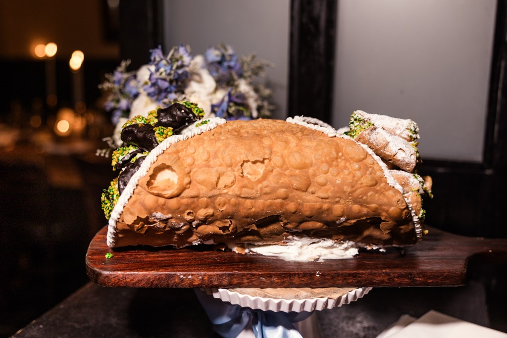 A giant cannoli filled with smaller cannoli, displayed on a wooden serving board with decorative flowers for wedding reception at Osteria Via Stato in downtown Chicago