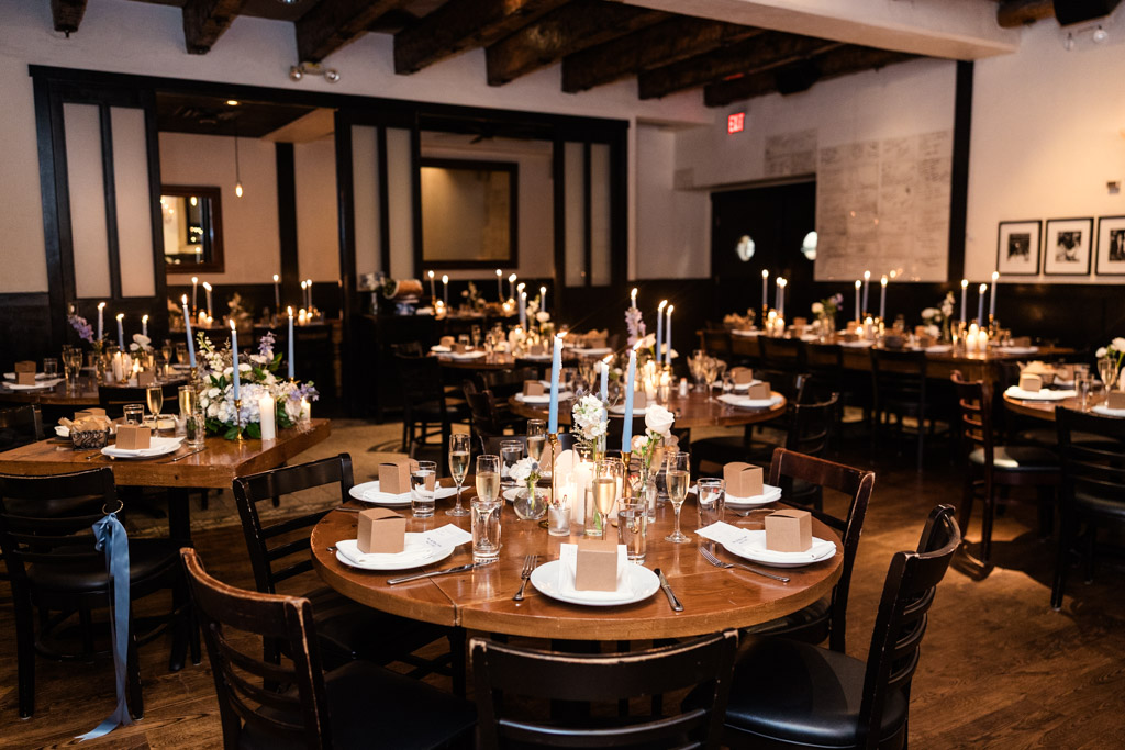 Osteria Via Stato wedding reception space with round tables, candles, flowers, and gift boxes