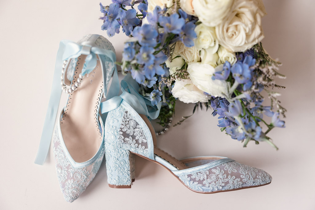 Bride's light blue lace shoes with ribbon and pearls beside a bouquet of white and blue flowers for wedding at Osteria Via Stato in downtown Chicago