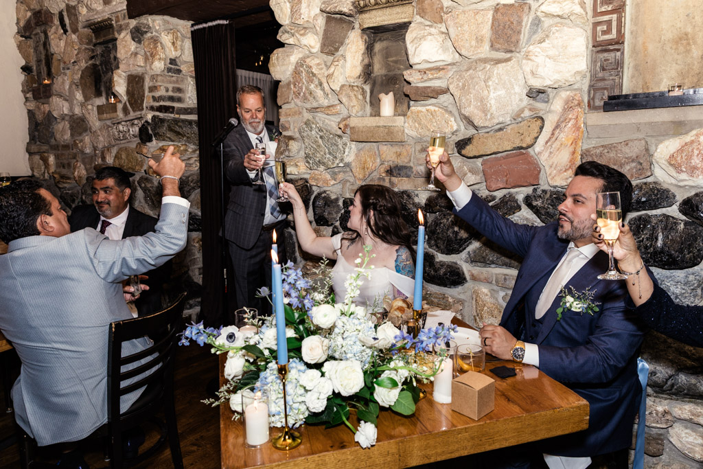 Bride, groom and guests in formal attire raise glasses for a toast during wedding reception at Osteria Via Stato