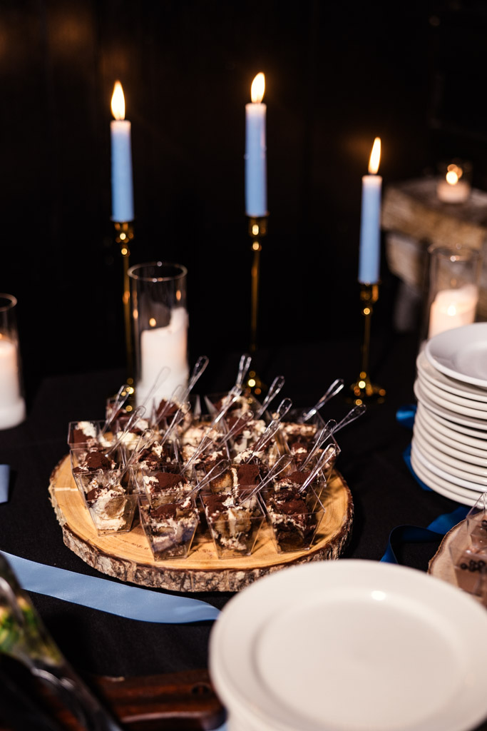 Mini dessert cups on a wooden tray at Osteria Via Stato, with blue candles and stacked plates in the background