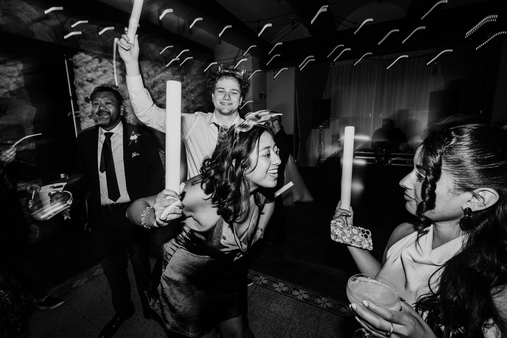 Guests celebrating during wedding reception at Osteria Via Stato, holding light sticks, smiling and dancing