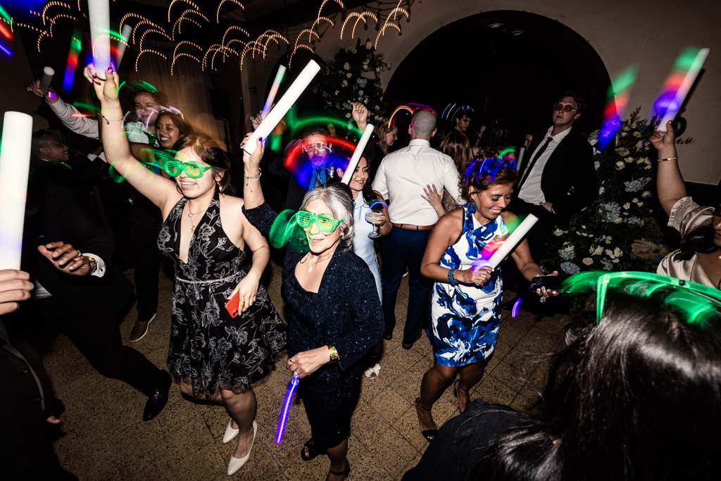 People dancing at a party with neon glow sticks and oversized glasses at Osteria Via Stato wedding reception