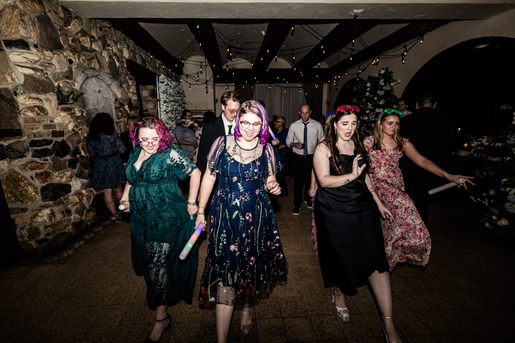 Guests in colorful dresses dance during a wedding reception at Osteria Via Stato, with others celebrating in the background