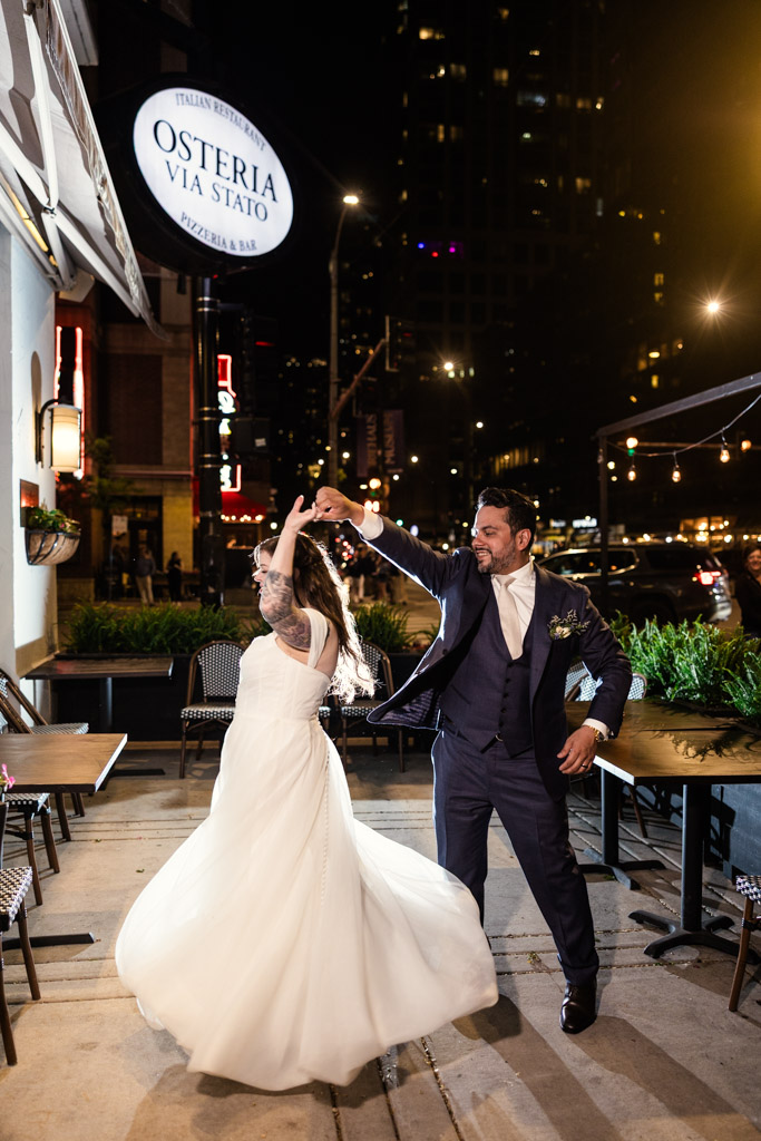 Newlyweds dance joyfully outside Osteria Via Stato at night, basking in the glow of city lights