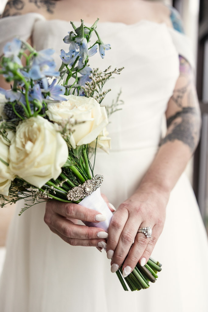Bride holding a bouquet of white and blue flowers showing her engagement ring