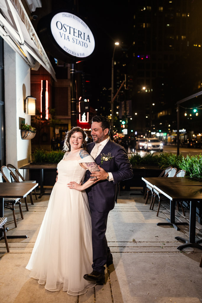 Bride and groom smiling and posing together at night outside Osteria Via Stato