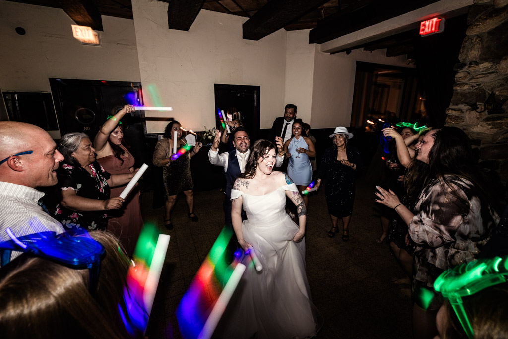 Bride and groom dance joyfully at Osteria Via Stato, surrounded by guests waving colorful light sticks