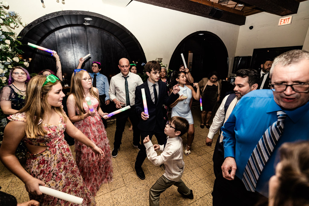 Guests in formal attire dance and hold glowing sticks at Osteria Via Stato wedding celebration