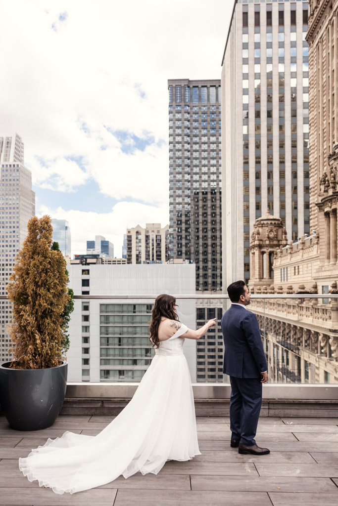 A bride in a white dress approaches a groom in a blue suit during their first look on the rooftop of Virgin Hotels Chicago
