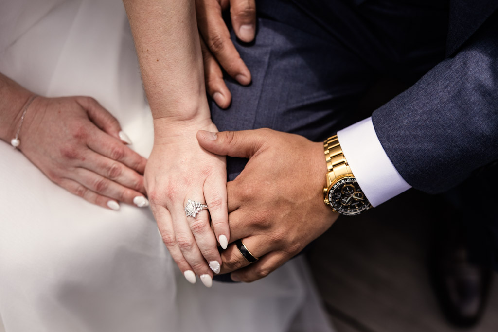 Close-up of a couple's hands with wedding rings, one wearing a gold watch and the other adorned with a sparkling diamond ring