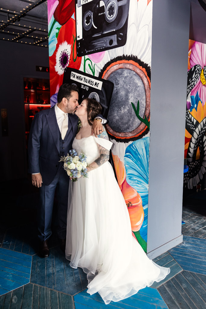 Bride and groom kiss in front of a colorful, flower-filled mural at Virgin Hotels Chicago