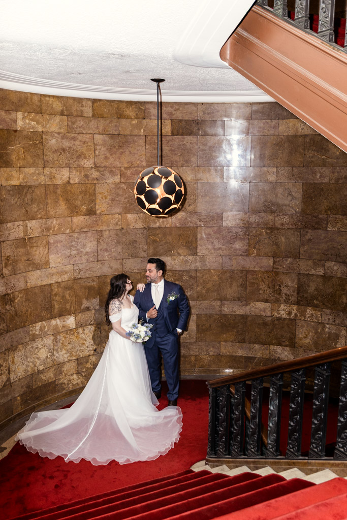 Bride and groom smiling at each other on a red-carpeted staircase under a modern pendant light at Virgin Hotels Chicago