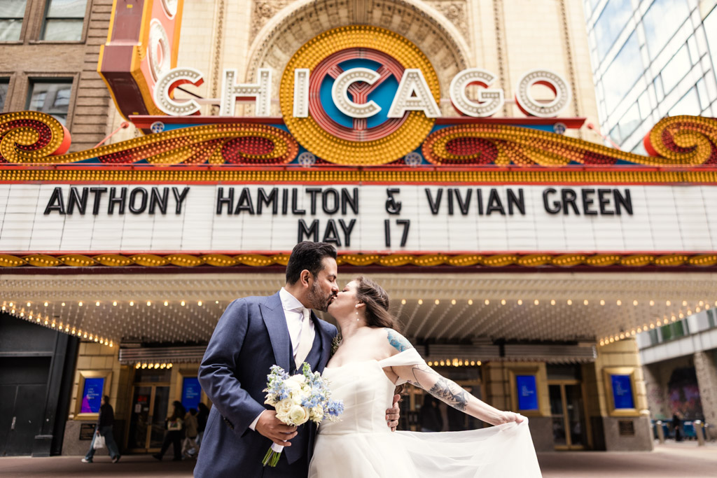 A couple kisses in wedding attire under the Chicago Theater marquee before heading to Osteria Via Stato for their wedding celebration