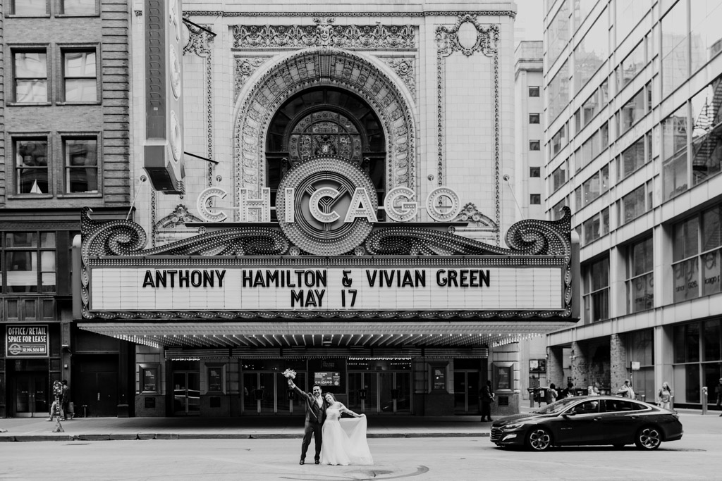 Black and white photo of bride and groom posing in front of the Chicago Theatre marquee