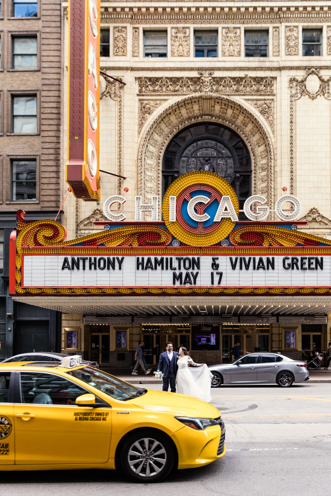 A bride and groom cross the street in front of the Chicago Theatre marquee before their Osteria Via Stato wedding celebration