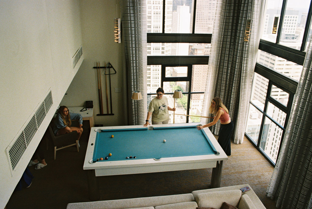 Film photo of three people in a modern high-rise hotel room at Chicago Marriott Downtown Magnificent Mile playing pool near large windows with a city view