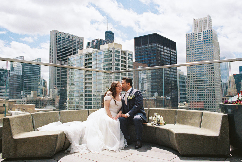 Film photo of bride and groom sitting on a rooftop lounge at Osteria Via Stato, with Chicago skyline in the background
