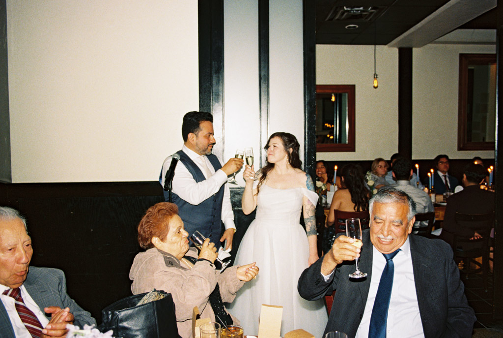 Film photo of bride and groom toasting with guests inside Osteria Via Stato restaurant during their wedding celebration