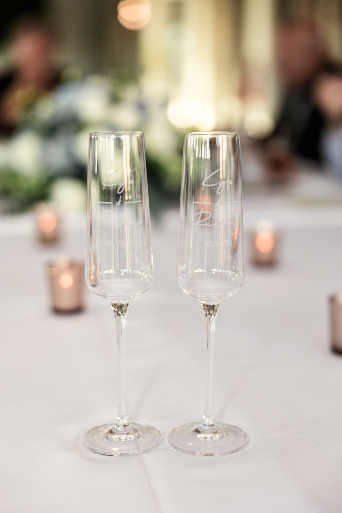 Two champagne flutes rest on a white tablecloth at The Drake, with candles flickering and blurred flowers in the background