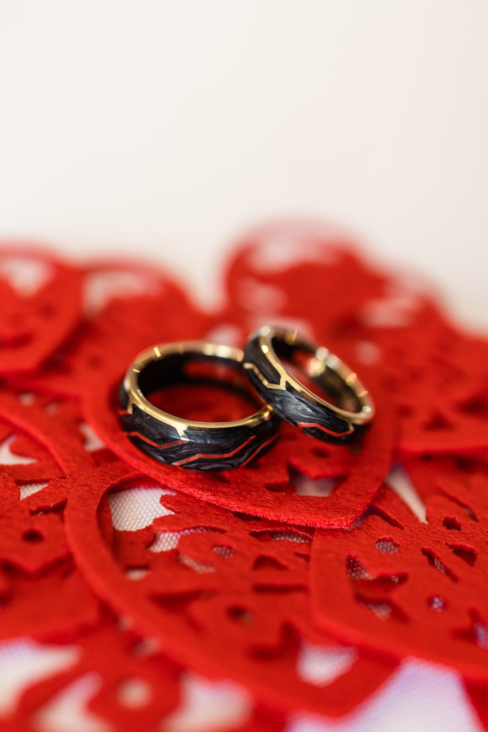 Two gold and black wedding rings on intricate red lace hearts for outdoor wedding ceremony at The Drake Oak Brook