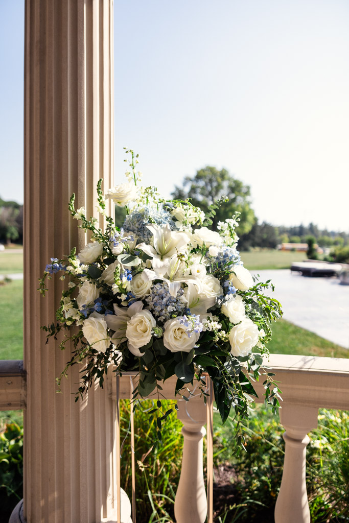 A large bouquet of white and blue flowers sits on a pedestal near a pillar for outdoor wedding ceremony at The Drake Oak Brook