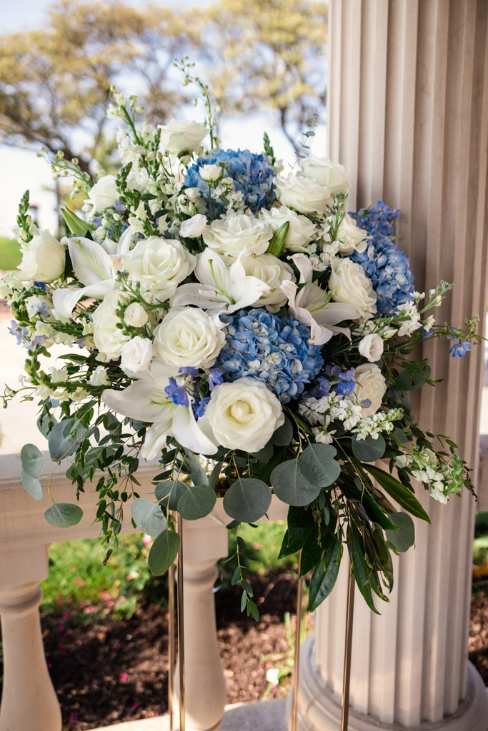 Floral arrangement with white roses, lilies, blue hydrangeas, and lush greenery by a column for The Drake Oak Brook outdoor wedding ceremony