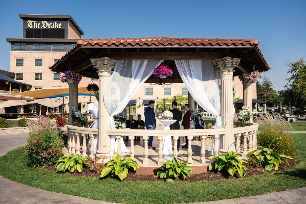 Grooms stand with officiant under a gazebo at an outdoor wedding ceremony at The Drake Oak Brook
