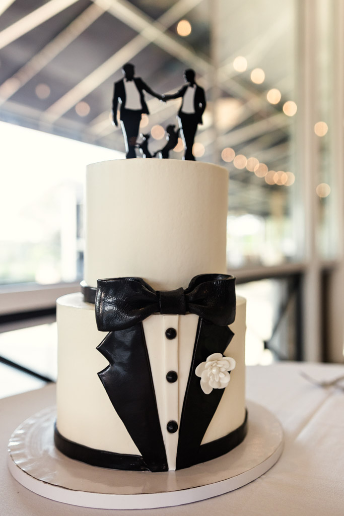 Two-tier wedding cake with tuxedo decorations, topped with two groom figurines holding hands for wedding celebration at The Drake Oak Brook