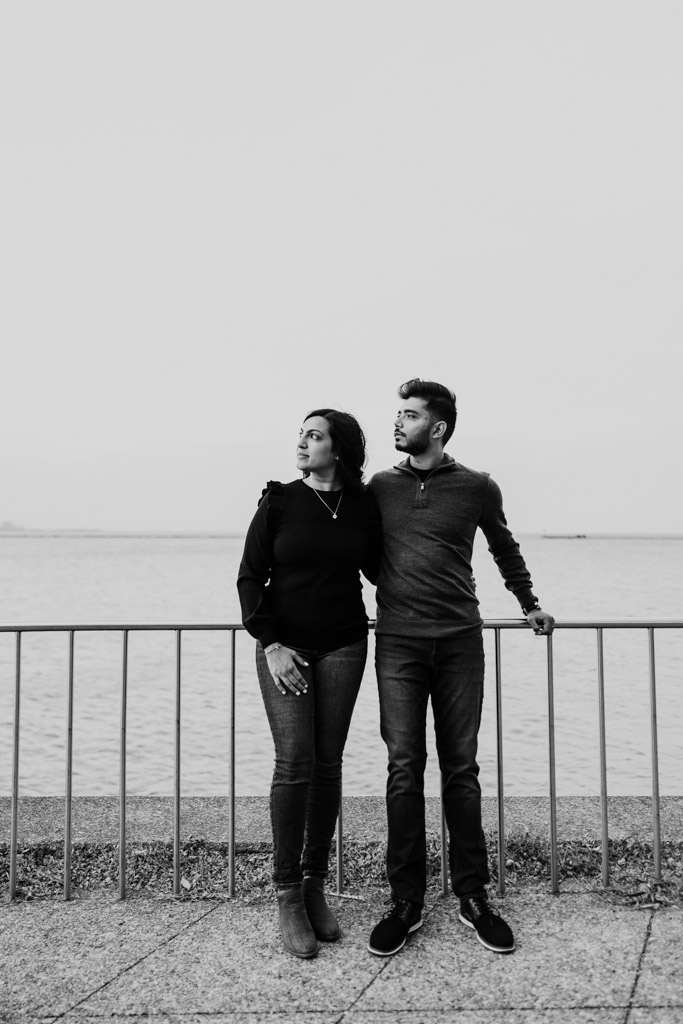 Black and white photo of woman and a man standing by a waterfront railing in Olive Park with Lake Michigan in the background during Chicago fall engagement session
