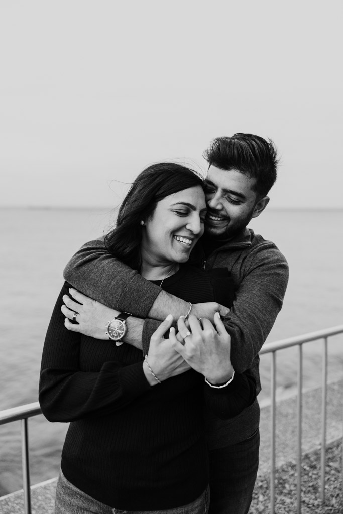 Black and white photo of smiling couple embracing by Lake Michigan during their Chicago fall engagement session